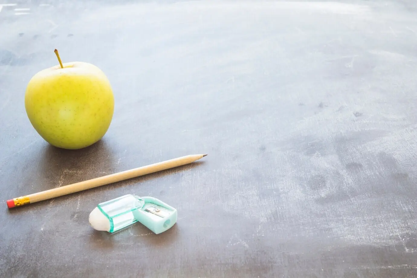 Tischplatte mit Stift, Apfel und Bleistiftspitzer.